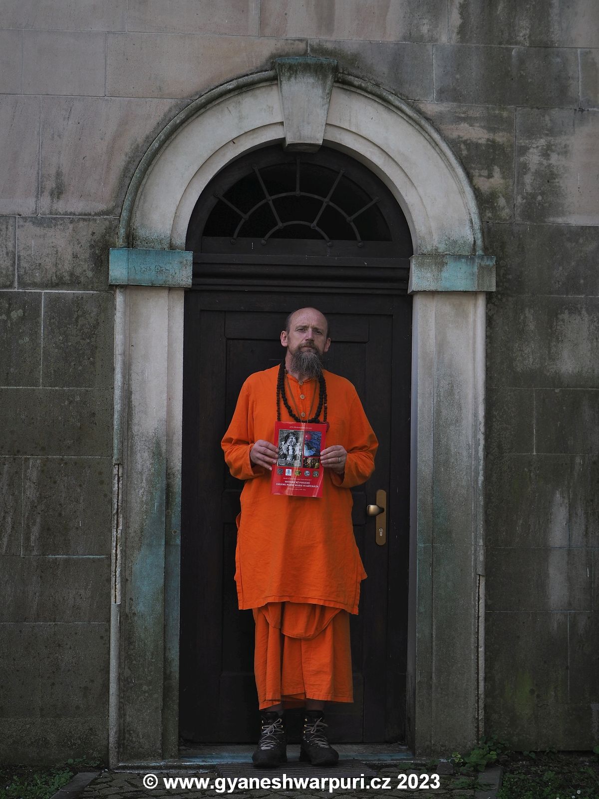 Svámí Gyaneshwarpuri drží Acta Speleohistorica Křtiny před vchodem do krypty chrámu Panny Marie ve Křtinách. Foto: Jiří Dressler 2023